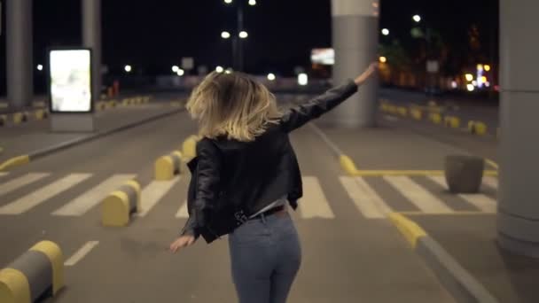 Glada blond kvinna att ha kul utomhus på natten. «««Kör, imitera planet. Klädd i jeans och svart jacka. Sällsynt vy — Stockvideo