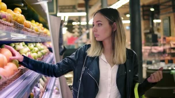 Πώληση, φαγητό, ψώνια, τον καταναλωτισμό και άνθρωποι έννοια. Ξανθιά γυναίκα επιλέγοντας τα φρούτα από τα πολύχρωμα ράφια για σούπερ μάρκετ — Αρχείο Βίντεο