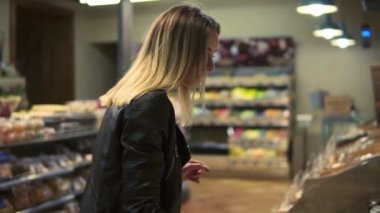 Kafkas kadın yiyecek satın almak karar vermekte süpermarkette iyi bakıyor. Ürünleri intobasket koyarak. Yan görünüm