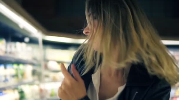 Au supermarché : joyeuse jeune fille drôle de danse entre les étagères dans le supermarché. Fille blonde portant un jean et une veste en cuir noir. Vue rapprochée — Video