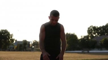 Genç kaslı adam kollarını ayakta açık havada stadyumda, ellerini sallayarak, eklem kadar ısınma sırasında germe