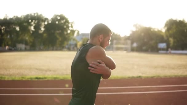 若い選手の男性の競技場でトラックに彼の手をストレッチ ランニングやトレーニングのための準備します。屋外で運動する白人男性の側面図 — ストック動画