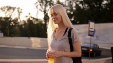 Tarafından Street yürüyüş gülümseyen, güzel uzun saçlı bir kadın. Siyah backbag ve yavaş yavaş yürüme, onun zaman zevk limonata fincan ile rahat kız. Yakın çekim.