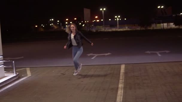 Donna veramente felice alla stazione di servizio in jeans e giacca nera di pelle che corre in giro di notte — Video Stock