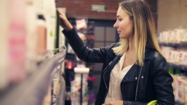 Gülümseyen beyaz kadın kozmetik bölümünde dükkanda siyah şişe şampuan raf ile toplama. Yan görünüm