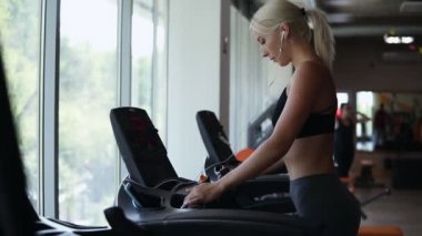 Sarışın kadın kulaklık müzik dinlerken koşu bandında yürüyüş üzerinde konsantre at kuyruğu ile uygun. Sağlıklı yaşam konsepti, spor aktivitesi