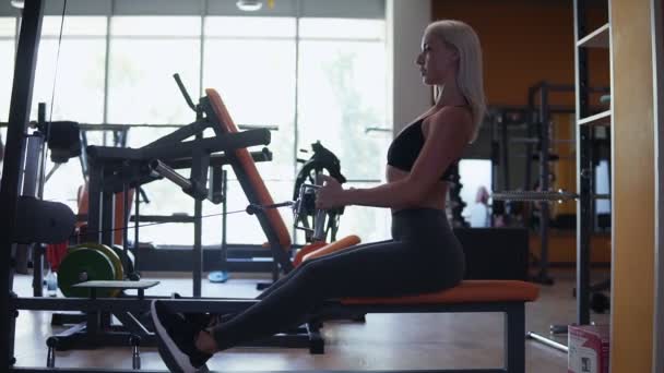 金髪の女性は、ジムで筋肉トレーニングを行うこと。スポーツ選手のトレーナーを重量を引いて、ジムでワークアウト — ストック動画