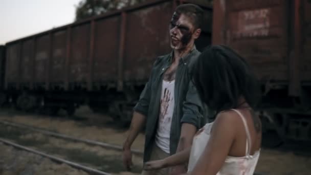 Dua hantu atau zombie dengan pakaian berdarah bermain-main dengan satu sama lain di luar ruangan saat berdiri di dekat gerobak kereta api. Hari waktu — Stok Video