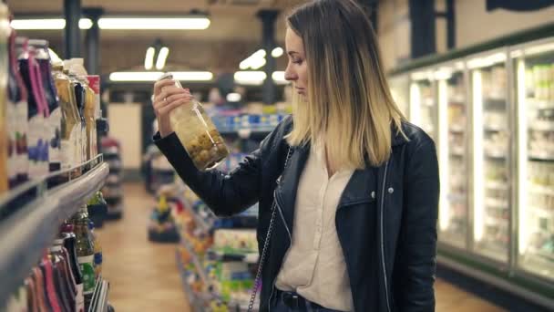 Вид сбоку улыбающейся женщины в супермаркете, которая выбирает сок в бутылке и кладет его в корзину. Блондинка улыбается женщина выбирает продукты в торговом центре — стоковое видео