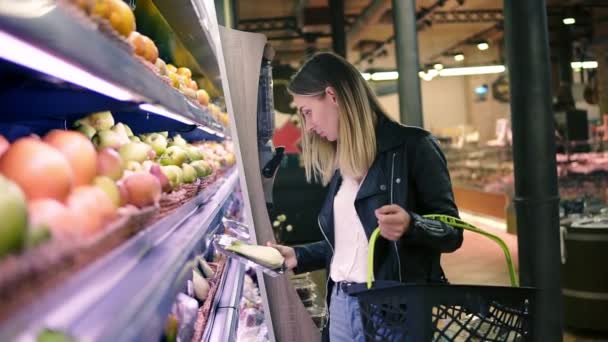 La mujer elige verduras en el supermercado. Mujer joven rubia elegir productos en el centro comercial. La chica está cerca del estante de la tienda. Vista lateral — Vídeo de stock