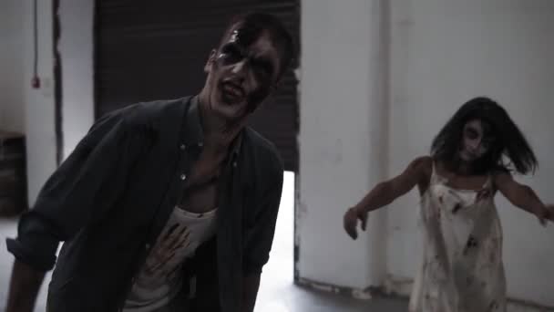 Espeluznante escena de dos zombis masculinos y femeninos entrando en posición vacía con paredes blancas. Halloween, filmación, escenificación. Persianas enrollables abiertas en el fondo — Vídeo de stock