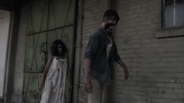Дві зомбі гуляють з покинутим будинком на фоні. Брюнетка дівчина з пораненим обличчям і кривавою білою сукнею і пораненим чоловічого зомбі виходять на вулицю. Прискорення кадрів — стокове відео