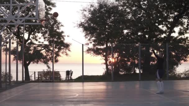 Stedicam felvételek egy fiatal lány, hogy egy lövés oldalról nettó kosárlabda. Szabadban a fák és a nap süt, a háttérben — Stock videók