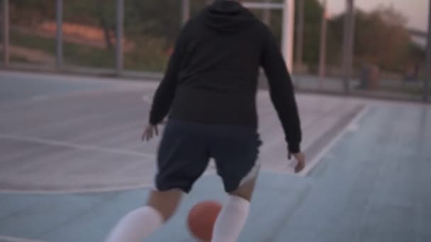 Backside footage of a young girl basketball player training and exercising outdoors on the local court. Dribbling with the ball, bouncing and make a shot — Stock Video