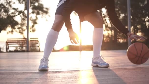 Açık sahada egzersiz genç kız basketbol oyuncusu. Zıplayan top düşük ayak bileği düzeyinde pratik. Güneş parlıyor ve arka plan üzerinde — Stok video