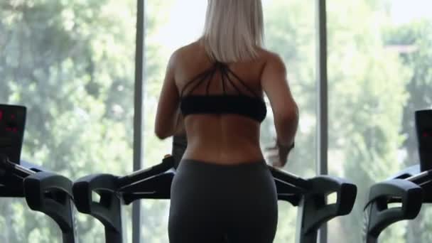 Fitness flicka kör snabbt på banan löpband i fitness-klubben, Blond flicka i sportkläder arbetande ute. Hälsosam livsstilskoncept, sportaktivitet — Stockvideo