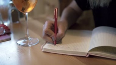 Uzun saçlı sarışın kadın modern bir kafede oturan ve düşünceli bazı notlar onun not defterinde yapma. Masada buz ile kokteyl bir bardak. Notebook amaçlı görüntüleri