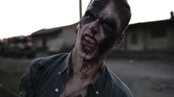 Retrato de un zombi macho con dientes ensangrentados y cara herida gritando y gritando. Halloween, filmación, escenificación. Borrosa ciudad abandonada en el fondo — Vídeos de Stock