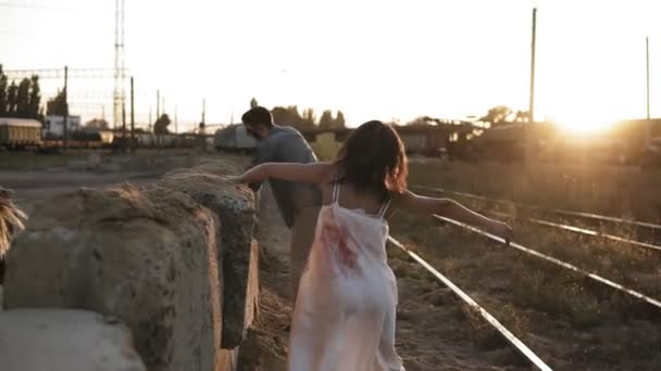 Immagine di inquietante fantasma maschile e femminile o zombie che cammina con la faccia ferita. zombie maschio arrampicata su blocchi a terra. Industriale, città abbandonata, strade ferrate intorno — Video Stock