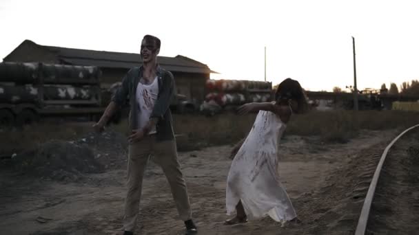 Espeluznante dos zombies en ropa ensangrentada caminando por la ciudad en ruinas durante el apocalipsis zombie. Lugar abandonado con camiones con misiles en el fondo — Vídeos de Stock