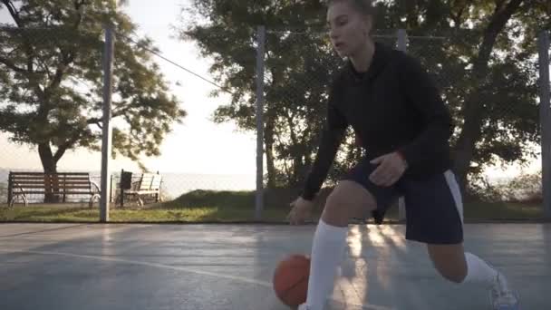 Filmagem de uma jovem jogadora de basquete treinando e se exercitando ao ar livre na quadra local. Dribbling com a bola, saltando e fazer um tiro. Movimento lento — Vídeo de Stock