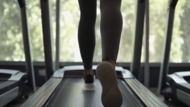 Sarışın, uygun kadın siyah sutyen ve spor salonunda panoramik pencerenin önünde bir koşu bandı üzerinde çalışan tozluk ağır çekim görüntüleri. Arka görünüm