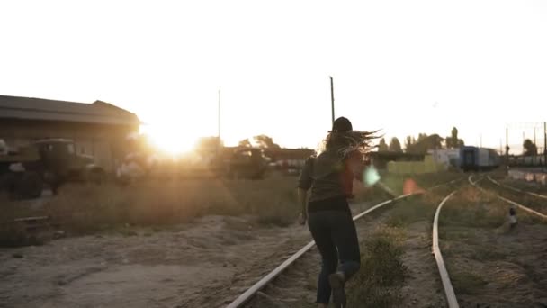 Mujer de pelo largo con gorra huyendo de un zombi espeluznante. Hombre y mujer zombi persiguiendo chica va por ferrocarril con una ciudad abandonada en el fondo — Vídeos de Stock