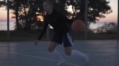 Teke tek oyunu oynarken kadın basketbolcu. Top runnung ve maling bir çember oyuncu. Açık havada.