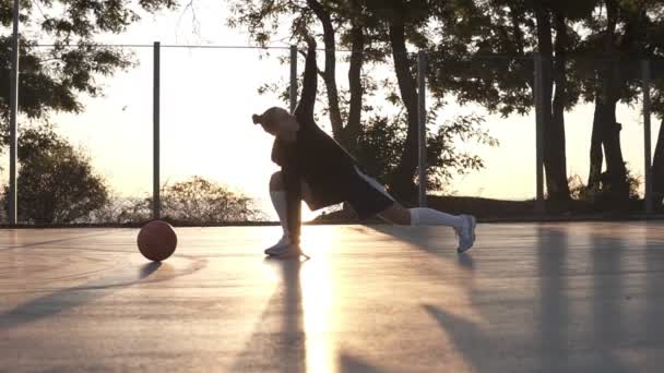 Beyaz Genç Kadın hoodie ve basketbol sahasına sabah ısınma şort yerleştirmek. Basketbol Eğitim önce bacaklarını germe. Sabah alacakaranlıkta — Stok video