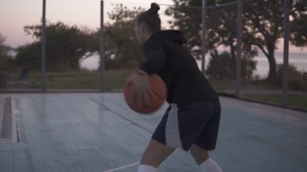 Filmrückseite einer jungen Basketballspielerin, die mit Ball auf dem Außenplatz joggt und ihn in den Korb wirft — Stockvideo