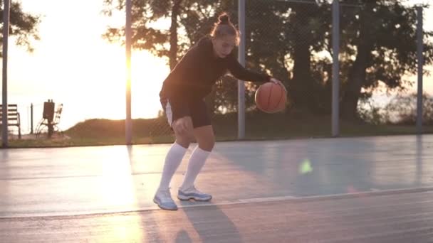 Κλείστε πλάνα από ένα νεαρό κορίτσι μπασκετμπολίστα να προπονείται και να γυμνάζεται στο γήπεδο. Νεαρή γυναίκα σε λευκές κάλτσες του γκολφ προπόνηση σταυρό γερός με μπάλα του μπάσκετ — Αρχείο Βίντεο