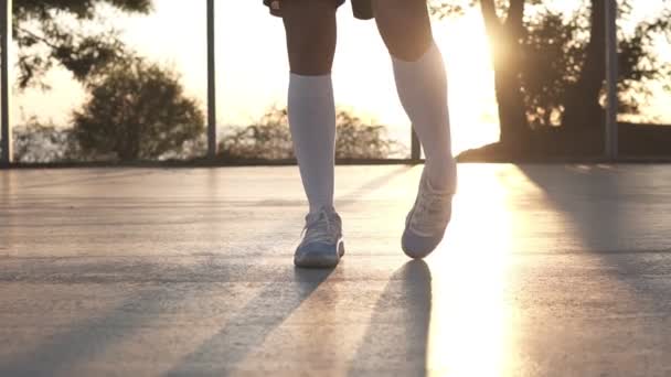 Молодая девушка вытягивает ноги в белых кроссовках и белых носках для гольфа на местной баскетбольной площадке. Неузнаваемые кадры с сияющим солнцем на фоне — стоковое видео