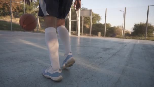 Rare view of a young girl basketball player training and exercising outdoors on the local court. Dribbling with the ball, bouncing and make a shot. Low angle footage — Stock Video