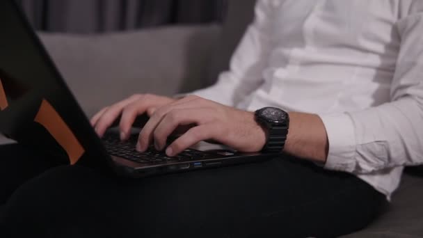 Syftar footage av mans händer att skriva på laptop. Klädd i svart elegant handwatches och vit skjorta. Ler kaukasiska man freelancer sitter i soffan i modern stil rum — Stockvideo