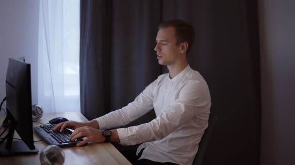 Casual affärsman arbetar hemma, sitter vid skrivbord, att skriva på tangentbordet, tittar på datorskärmen. Grå gardin i bakgrunden — Stockvideo
