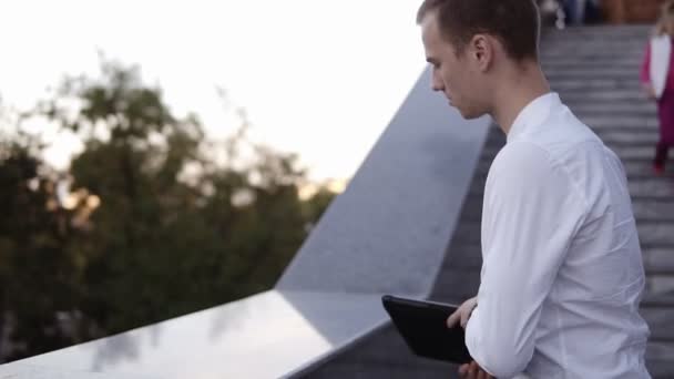 Kaukasische jongeman gestopt met fiets in de buurt van de trap zet zijn laptop op de bar en begint te werken wareless buitenshuis — Stockvideo