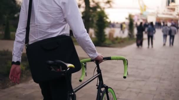 K nepoznání zamyšlený mladý podnikatel chůzi s kolo na ulici ve městě. Válcování jeho trekingové kolo na procházce v parku crowdy