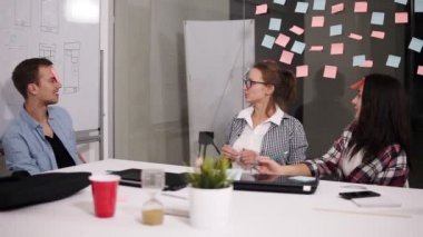 Üç genç arkadaşları modern loft office beyaz büyük beyaz tablosunda oturan grubunuz süre mola zamanı, alın ve kelime tahmin renkli kağıtlara sopa eğlenceli. Olumlu iş adamları