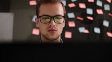 Bir dizüstü bilgisayar ofiste çalışan gözlüklü genç gülümseyen adam. İşadamı - ofis çalışanı. Erkek öğrenci iş yerinde bir bilgisayar. Cam geri otururken Internet üzerinde bilgi arama