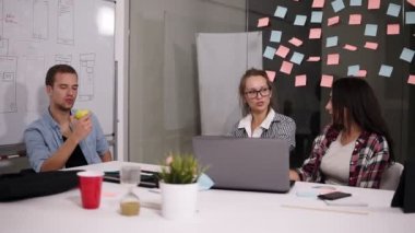 Genç adam ve yaratıcı çalışma alanı'ndaki office masada oturan iki kadın. Sarışın kadın onun vizyonu paylaşan. Adam bir elma yeme. Proje sorular nonformal şekilde tartışıyor.