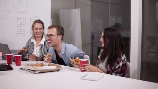 Fiatal kaukázusi munkatársai ebédelni break pizzát eszik együtt hivatalban. Nevetett, beszélt, szórakozás. Munkatársak felüdítő után befejező munkák — Stock videók