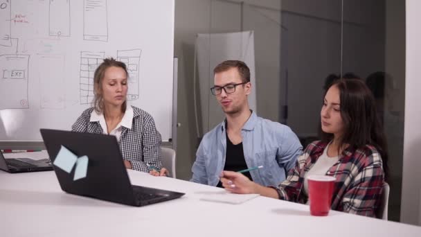 Tomando grandes decisiones. Joven con gafas haciendo gestos con un lápiz y discutiendo algo con sus compañeros de trabajo escuchándolo sentado en la mesa de la oficina en un lugar de trabajo creativo — Vídeo de stock