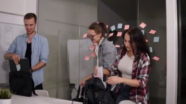 Gençlerin grup çanta ve dizüstü bilgisayarlar ve belgeleri ile birlikte office için işe gelmek iken gülümseyerek olumlu. Cam duvar yapışkan renkli kağıtlar ile başa ayakta