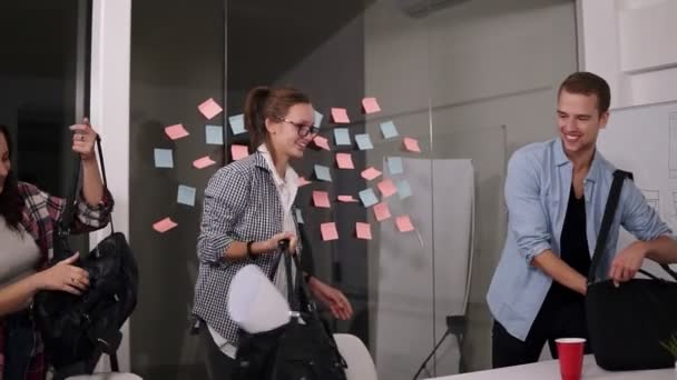 Grupo de jóvenes positivos sonriendo mientras vienen a trabajar a la oficina junto con bolsas y papeles de pie de nuevo a la pared de vidrio con papeles coloridos pegajosos. Movimiento lento — Vídeo de stock