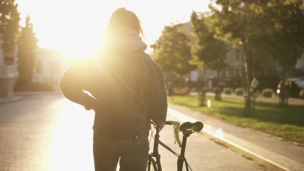 市の道路で自転車に乗って横に歩いている女性。女性自転車ライダーの街の通りの上を歩きます。舗装された通り美しい街で自転車と一緒に歩いている女性の概要ショットを閉じます。太陽が輝く — ストック動画