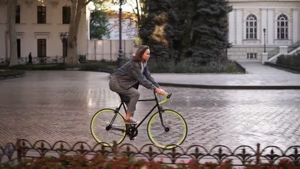 Mujer montando en bicicleta en la ciudad camino pavimentado. Mujer ciclista tener un paseo en la mañana. Calle de la ciudad vacía con un hermoso edificio antiguo en el fondo — Vídeo de stock