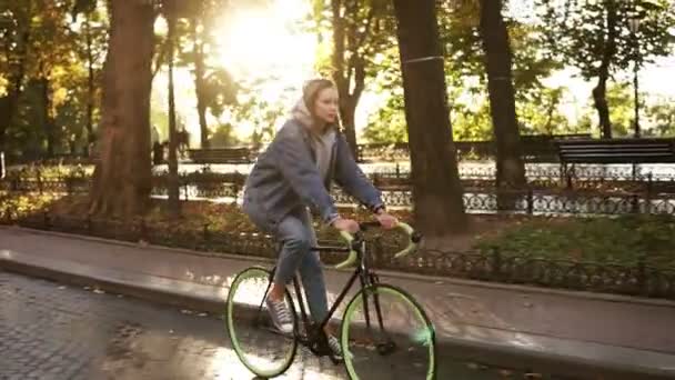 Mooie Kaukasische vrouw een fiets in de ochtend park of boulevard. Zijaanzicht van een jonge vrouw met een trekking fiets, het dragen van sneakers en casual kleding. Slow motion — Stockvideo