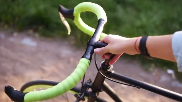 Aufnahmen von oben zeigen eine junge Frau, die neben einem Fahrrad im morgendlichen Park oder auf dem Rasen spaziert. das Mädchen, das mit ihrem Trekkingrad geht und ein grün gefärbtes Ruder hält — Stockvideo