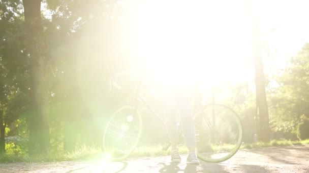 Przemyślane dziewczyna, opierając się na jej trekking z green kolorowe koła. Patrząc na jej telefon komórkowy, nosić jasne ubrania casual. Drzewa, słońce mocno świeci na tle, żaluzje obraz — Wideo stockowe