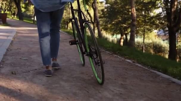 Primer plano de las imágenes de la mujer en zapatillas de deporte caminando junto a una bicicleta en el parque de la mañana o la calle. Vista rara de una joven caminando con su bicicleta de trekking por carretera pavimentada — Vídeos de Stock